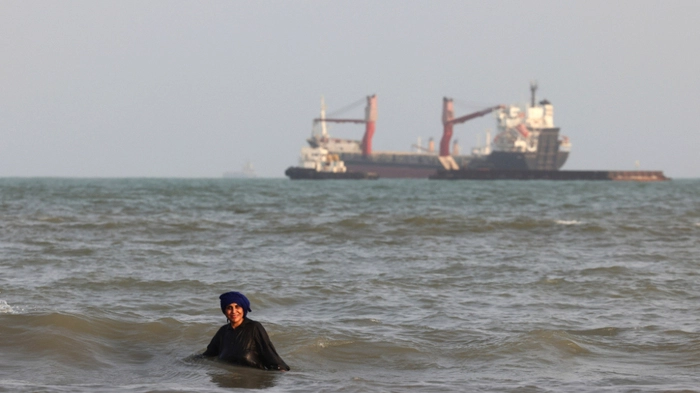 An Iranian women enjoy a dip in the sea as vessels are seen in the Strait of Hormuz off the port city of Bandar Abbas, in southern Iran on August 10, 2026. The US President signalled on August 9 that he was prepared to let economic pressure mount against Iran, apparently backing away from more military strikes after Tehran issued a list of demands for opening the Strait of Hormuz. His remarks came after Iran issued over the weekend a list of conditions to reopen the Strait of Hormuz, which has remained largely closed since the start of the Middle East war in late February. (Photo by Atta KENARE / AFP) /
