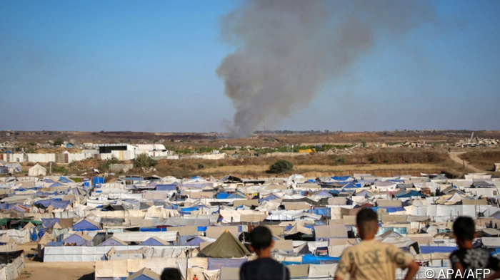 Children watch from atop a promontory overlooking shelters for people displaced by war, as smoke billows in the background near the Nuseirat camp for Palestinian refugees in the central Gaza Strip on June 19, 2026. Palestinian Islamist movement Hamas on Monday hailed a deal between the United States and Iran, expressing hope it would help put an end to violence in the Gaza Strip. Israel and Hamas trade near-daily accusations of truce violations and the Gaza Strip remains gripped by bloodshed as progress on permanently ending the war remains stalled. (Photo by Eyad Baba / AFP)