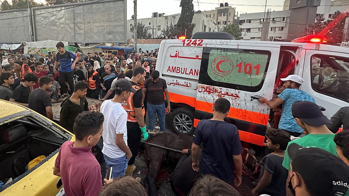  Ein beschädigter Krankenwagen mit Blutflecken auf der Türe inmitten einer Menschenmenge. | Der Beschuss eines Rettungskonvois sorgt für Bestürzung. 