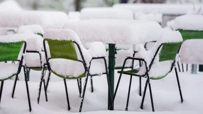 Grüne Stühle und Tische in einem Gastgarten, mit mehreren Zentimetern Schnee bedeckt
