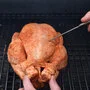 Person steckt Thermometer in ein Grillhuhn.