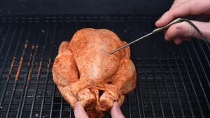 Person steckt Thermometer in ein Grillhuhn.