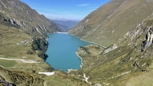 Blau schimmernder Stausee, umgeben von grünbewaldeten Bergen
