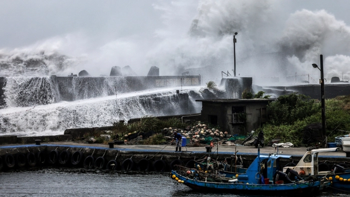 Fischerboote liegen in einem Hafen, dahinter treten Wassermassen über Mauern.