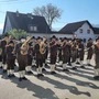 Eine große  Blasmusikkapelle steht auf einem Platz in der Sonne und spielt