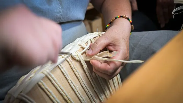 Frauenhände flechten Stränge aus Stroh an einem Korb ineinander