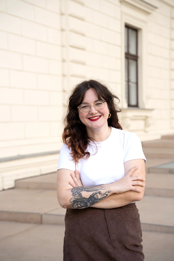Portrait einer jungen Frau mit dunklen Haaren und Brille in weißem T-Shirt und schwarzem Rock