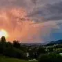 Blick über Graz zeigt eine gewaltige Regenwolke mit Blitzen im Inneren, dahinter die untergehende Sonne