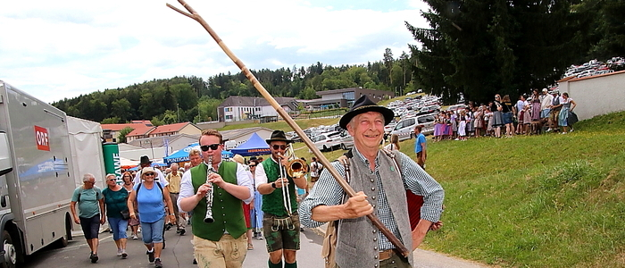 Mann mit Wanderstock, dahinter Musikanten