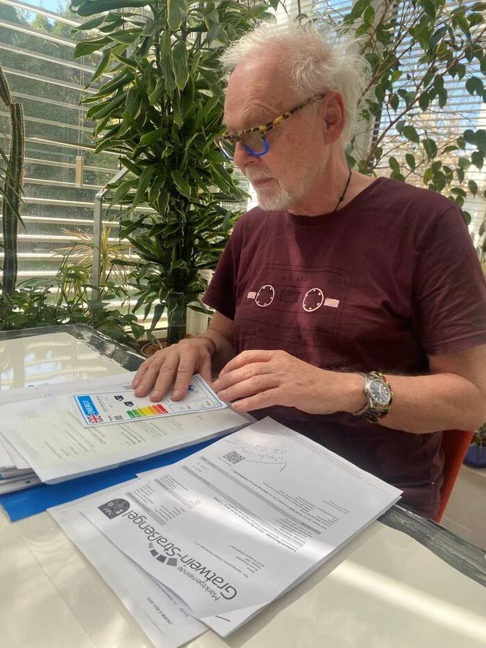 Ein älterer Mann sitz vor Unterlagen zur genehmigung. Im Hntergrund stehen Pflanzen