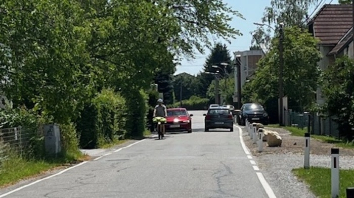 Zwei Autos kommen sich am Neufeldweg entgegen. Vor einem fährt ein Mopedfahrer. Durch die Poller rechts und Zäune links bleibt kaum Platz , um auszuweichen oder zu Fuß zu gehen.