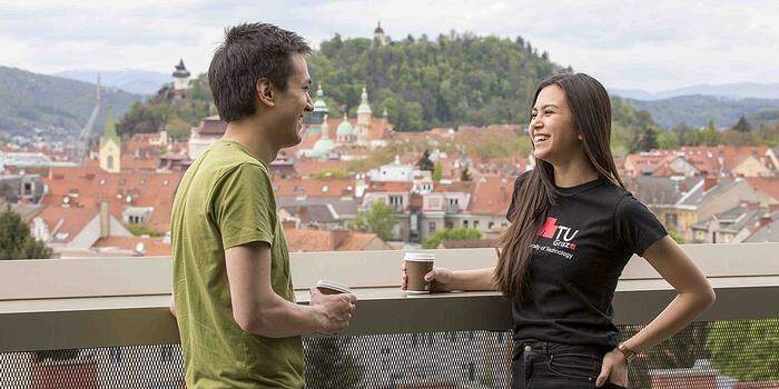 Zwei junge Studenten auf der Dachterrasse mit Blick über Graz, hinten der Schloßberg | Mensa Rooftop am Campus Neue Technik der TU Graz