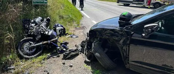 Foto vom Unfallort: Das Motorrad liegt schwer beschädigt am Straßenrand, auch die Front des Pkw ist beschädigt