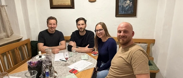Gruppenfoto der zufällig zusammengewürfelten Gruppe an einem Tisch in einem rustikal eingerichteten Wirtshaus