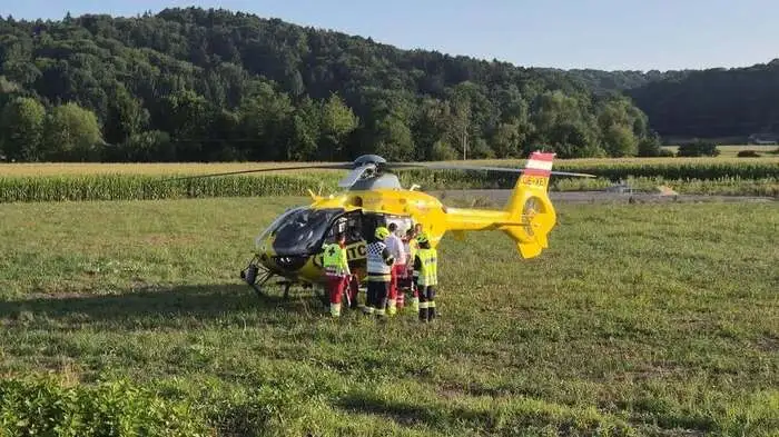 Gelber Rettungshubschrauber steht in einem Acker, Mitarbeiter vom Roten Kreuz mit den gelb-roten Uniformen