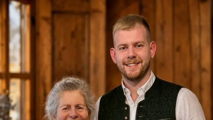 Ein Mann und seine Mutter posieren für ein Foto. Die beiden tragen traditionelle Tracht