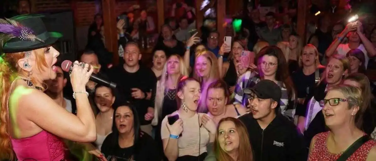 Foto aus dem Lokal: Sängerin Hannah mit Trachtenhut und rosa Kleid singt auf der Bühne, unten stehen die Fans