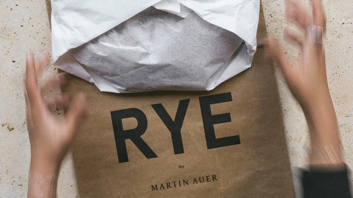Eine Person legt einen eingepackten Brotlaib auf ein Papiersackerl auf dem „Rye by Martin Auer“ steht