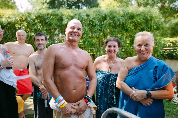 Ein Mann und eine Frau posieren für ein Foto. Sie lächeln gut gelaunt in Richtung Kamera. Im Hintergrund stehen eine weitere Frau und zwei Männer.