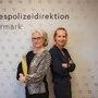 Zwei Frauen, Chefinspektorin Tanja Mannsbart und Abteilungsinspektorin Jasmine Schober, stehen Rücken an Rücken vor einer Stellwand mit der Aufschrift Landespolizeidirektion Steiermark | Seit 20 Jahren ein Team: Chefinspektorin Tanja Mannsbart und Abteilungsinspektorin Jasmine Schober