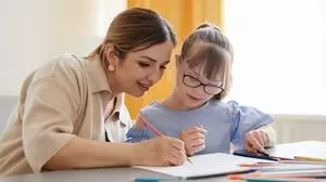 Portrait of cute girl with down syndrome studying at home with caring mother helping her in cozy interior