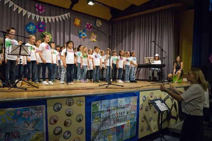 Die Klassen 2a und 2b eröffneten der Liederreigen, begleitet von den Blockflötenkindern, Waldhorn, Keyboard und Cajón. Jinder der ersten Klassen führten mit Tanz, Liedern, einem großen Blumenplakat, und Gartenwerkzeug die Besucher musikalisch auf eine Blumenwiese und verbreiteten den Duft von Frühling. Die 3. und 4. Klassen vollendeten den Liederabend. Als Solistin trat Sophie Reishofer mit dem Song Husavik (My Hometown) auf die Bühne.