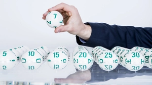 Eine Hand hält eine Lottokugel, darunter sind mehr Lottokugeln mit unterschiedlichen Zahlen zu sehen