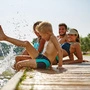 Familie sitzt auf einem Steg am See und badet glücklich mit den Füßen im Wasser