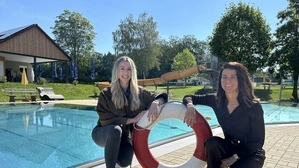 Lisa Peyer (links) und Daniela Zrim (rechts) kniend vor dem Pool des Freibades Söchau, in ihrer Mitte ein rot-weißer Rettungsring