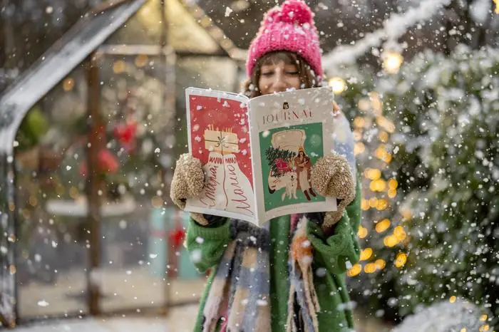 Young woman reads some magazine on New Year's theme at snowy backyard decorated for a winter holidays. Publishing for New Year holidays concept