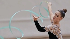 Eine junge Frau trägt einen schwarz-silbernen Glitzerturnanzug und bringt führt eine Übung mit einem hellblauen Gymnastikband aus