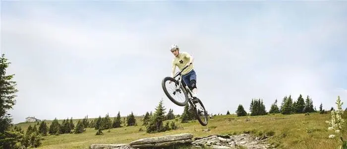 Ein Mountainbiker springt mit seinem Rad über eine Steinplatte auf einem Berghang