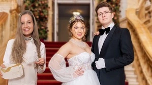 Zwei Frauen, eine in weißer Bluse, eine in weißem Ballkleid, und ein Mann in Anzug und Fliege sind vor einer Feststiege mit rotem Teppich zu sehen