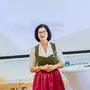 Frau mit kurzem, schwarzem Haar steht in einem grünen Dirndl mit roter Schürze vor einem digitalen Whiteboard an einem weißen Stehtisch