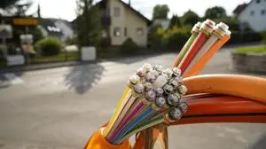 Ein Hand hält Glasfaserkabel in der Luft, im Hintergrund sieht man verschwommene Häuser | Die ländliche Region wartet auf schnelles Internet