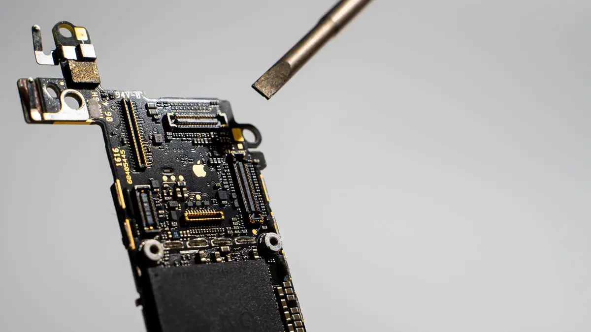 Kyiv, Ukraine - August 25, 2023: A screwdriver points to the golden Apple logo on the iPhone SE motherboard, close-up