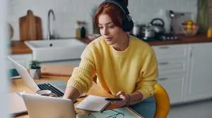 Beautiful woman in headphones using technologies while sitting at the kitchen counter