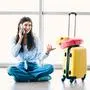 A young woman seated on the floor at an airport terminal window, talking on her phone and with a yellow suitcase packed for travel. She exudes excitement about her upcoming journey.