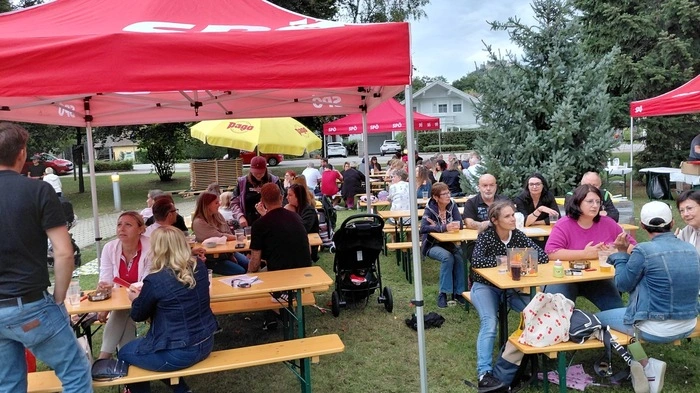 Menschen sitzen unter roten Sonnenschirmen auf Bierbänken